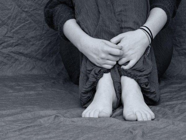 Osoba siedzi na podłodze i obejmuje rękami podwinięte nogi. Fot. pixabay.com