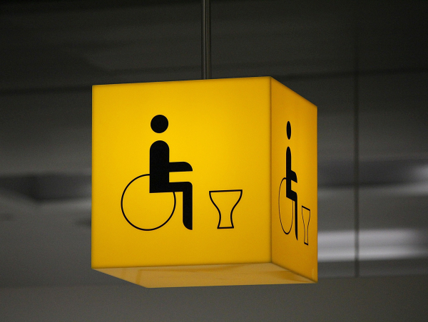 Żółty piktogram z osobą poruszającą się na wóżku oraz niedostosowana do jego potrzeb muszla klozetowa. Fot. pixabay.com