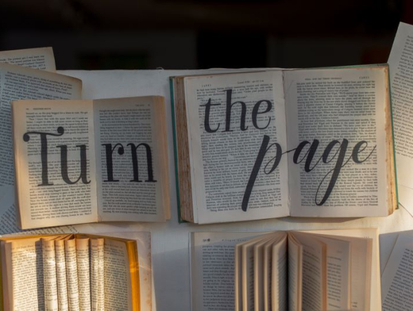 Tekst po angielsku „Turn the page” napisany na kartach rozłożonych na blacie książek