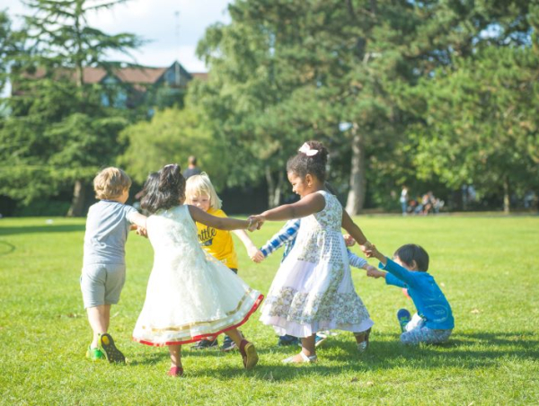 Grupa dzieci trzymających się za ręce w kółku, biegających na trawie