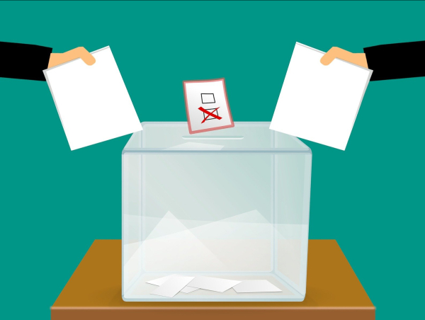Urna wyborcza, do której dwie ręce wrzucają kartki z głosami. Fot. Pixabay.com
