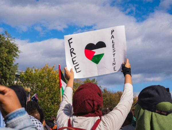 Tłum ludzi. Osoba z przodu odwrócona tyłem trzyma kartkę z flagą Palestyny w kształcie serca i hasłem Free Palestine