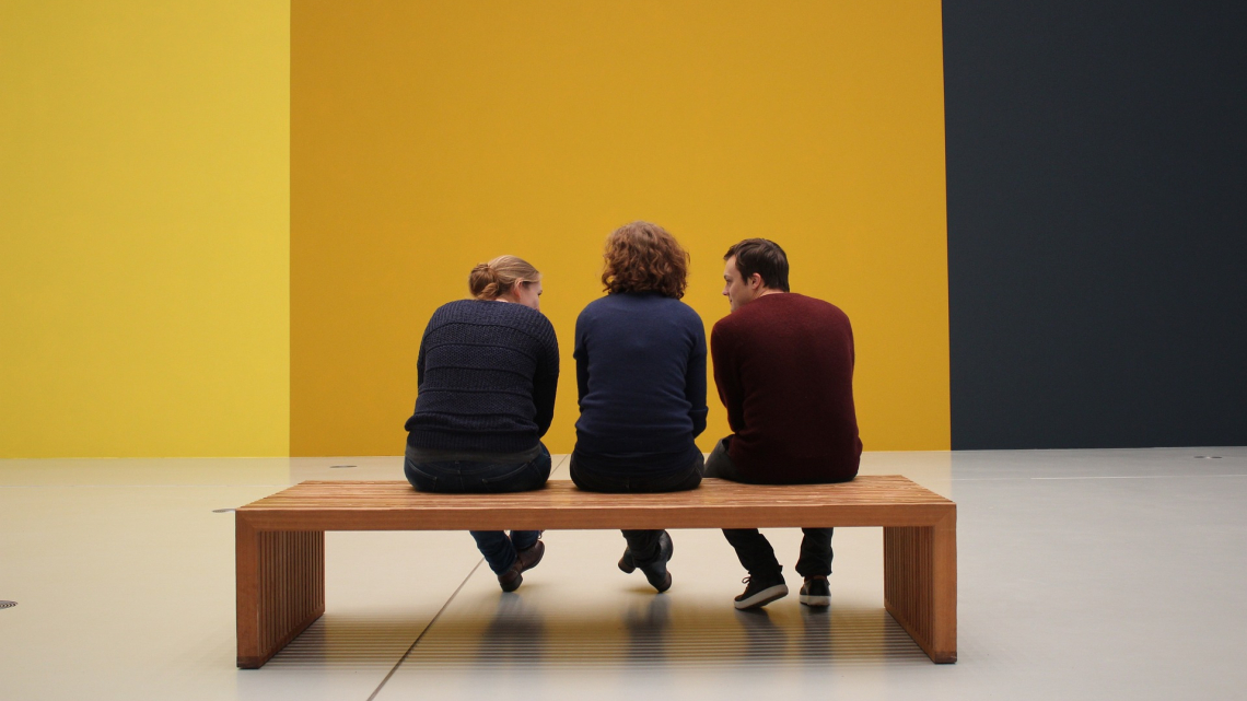 Trzy osoby siedzą na ławeczce na przeciwko kolorowej ściany. Fot. pixabay.com